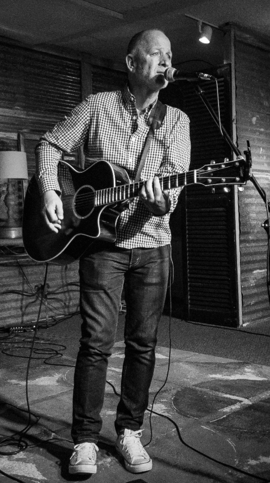 Black-and-white photo of Danny Dukes singing and playing acoustic guitar on stage
